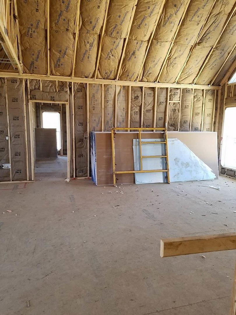 Unfinished room with exposed wood framing, yellow ladder leaning against wall, bags of cement on floor, visible ceiling beams and wood shelf