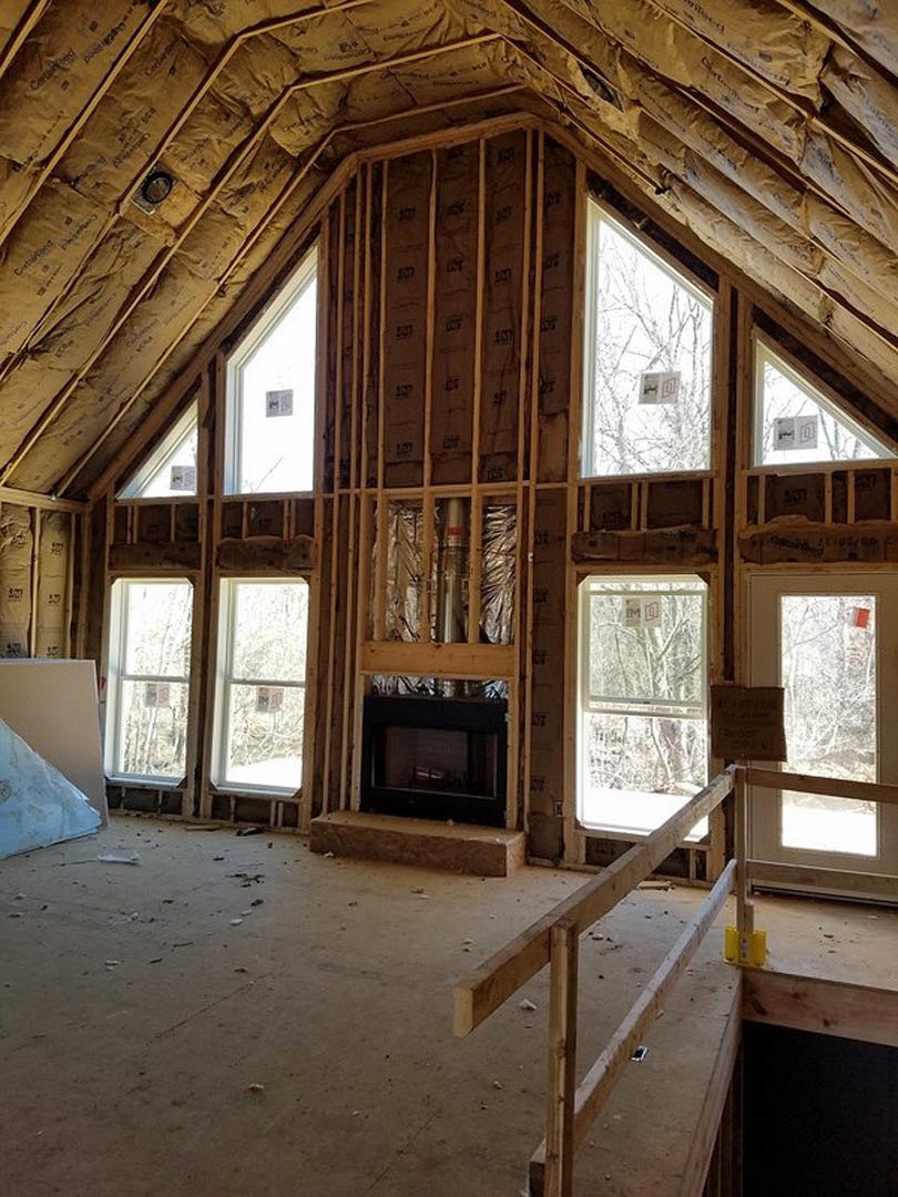 Living room with white walls, exposed wooden ceiling beam, stone fireplace, and large windows letting in natural light
