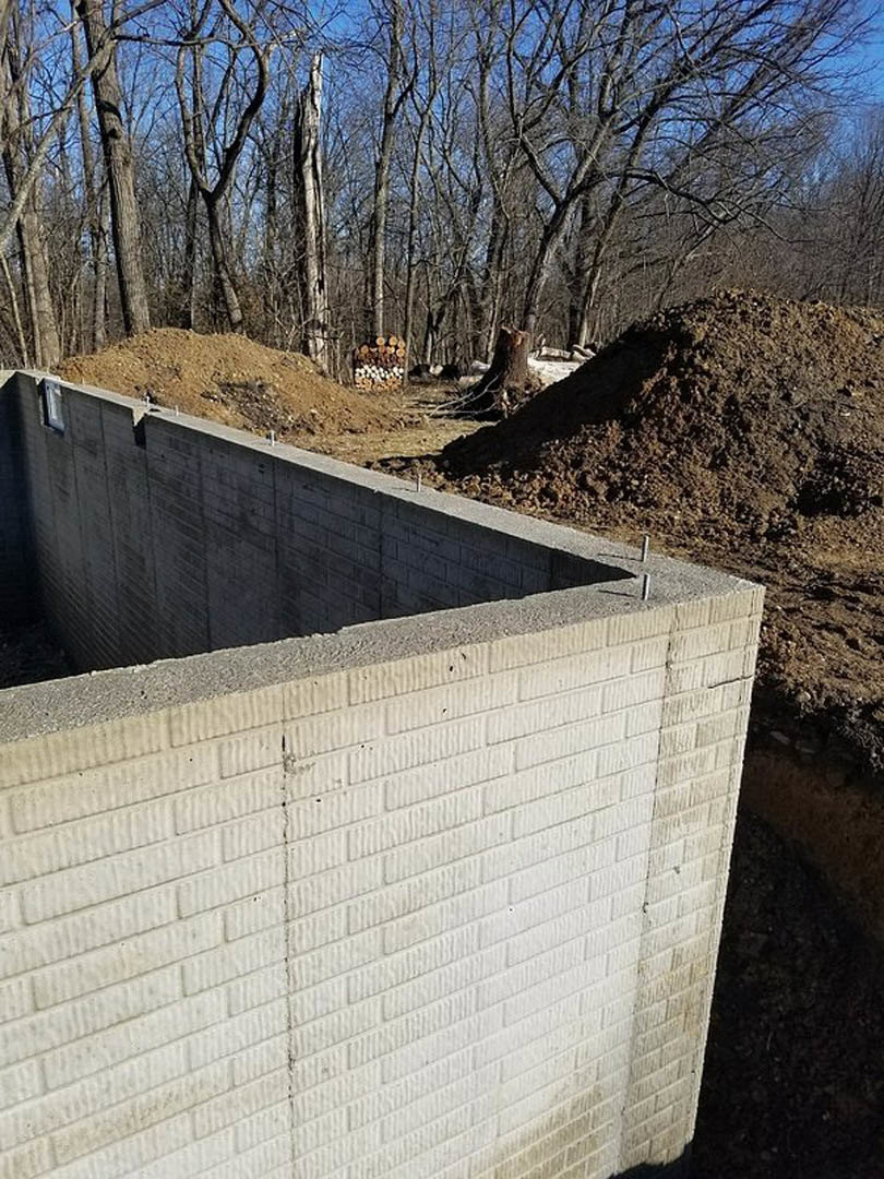 Smooth concrete retaining wall bordered by loose dirt and mature trees under a clear blue sky