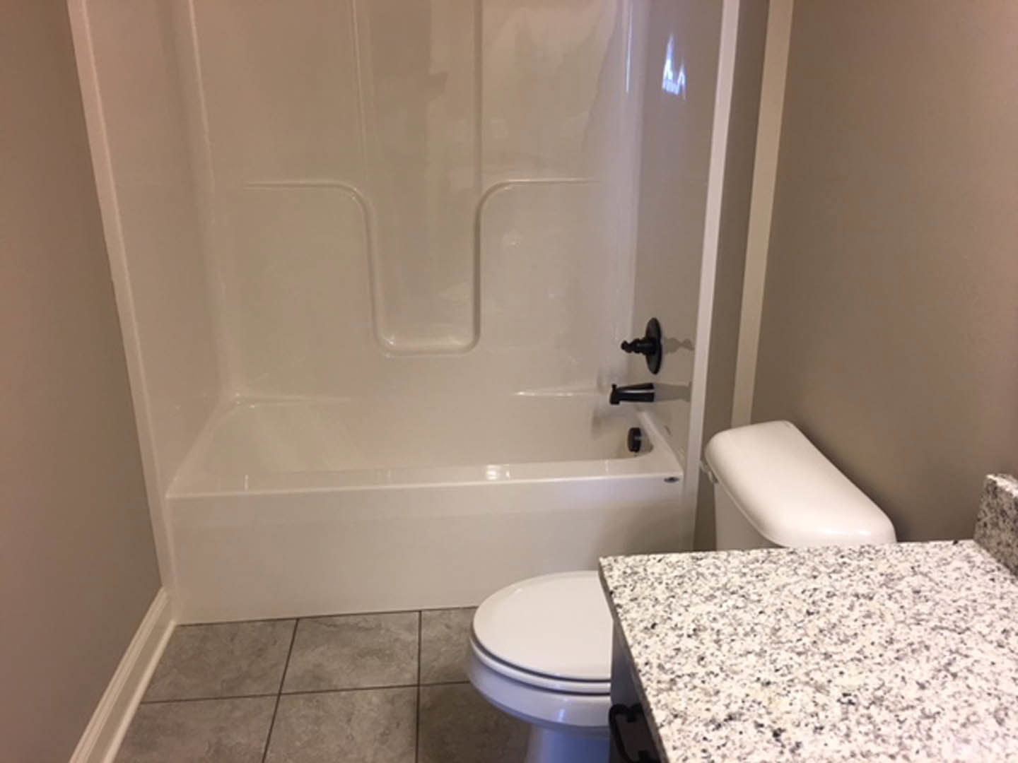 Marble countertop with undermount sink, white toilet, freestanding bathtub, light tile flooring, and neutral wall tiles in a modern bathroom.