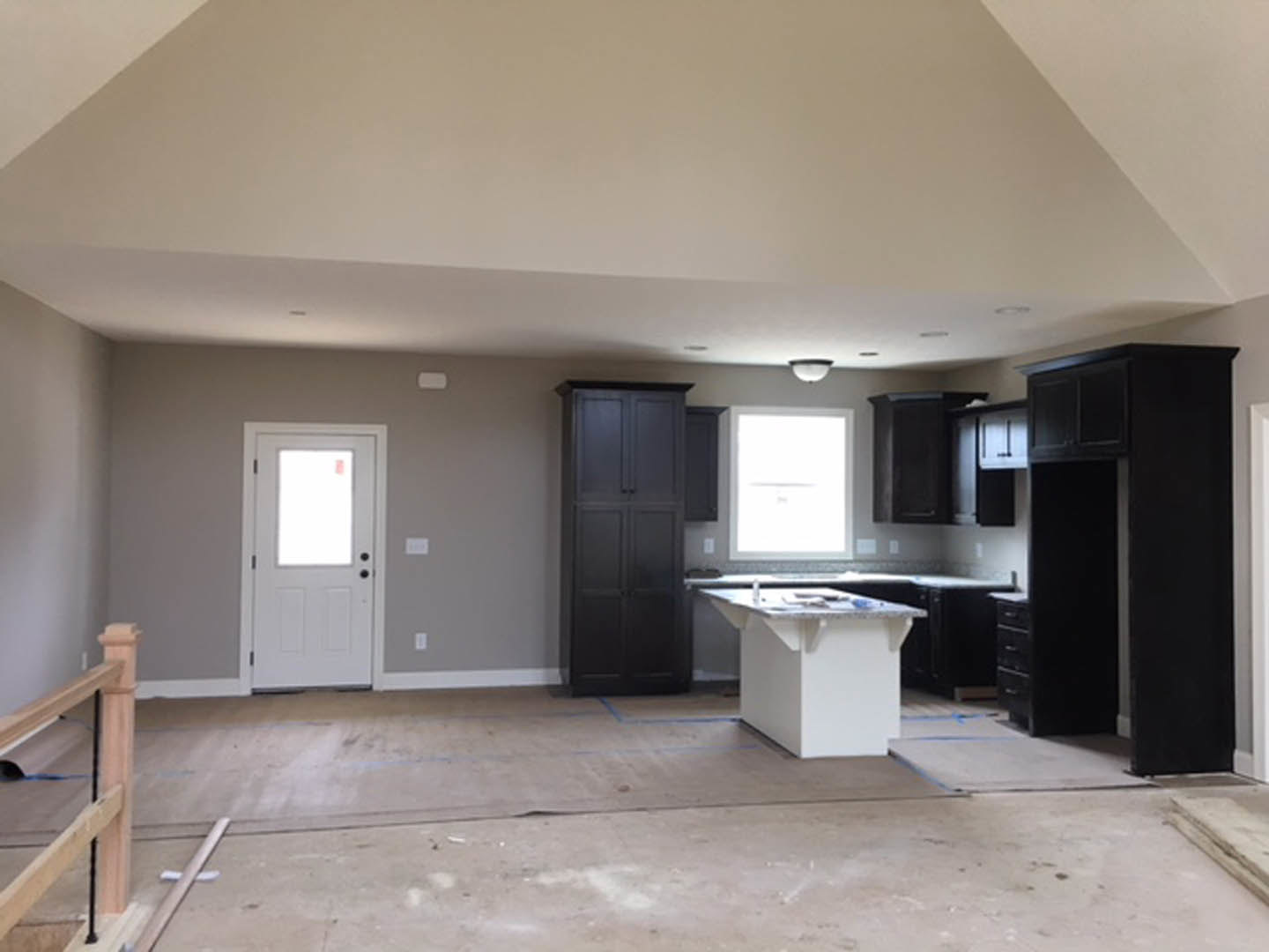 Kitchen featuring a white marble-topped island, dark cabinetry with metallic handles, light plaster walls, wood-framed windowed door, and modern lighting fixture.