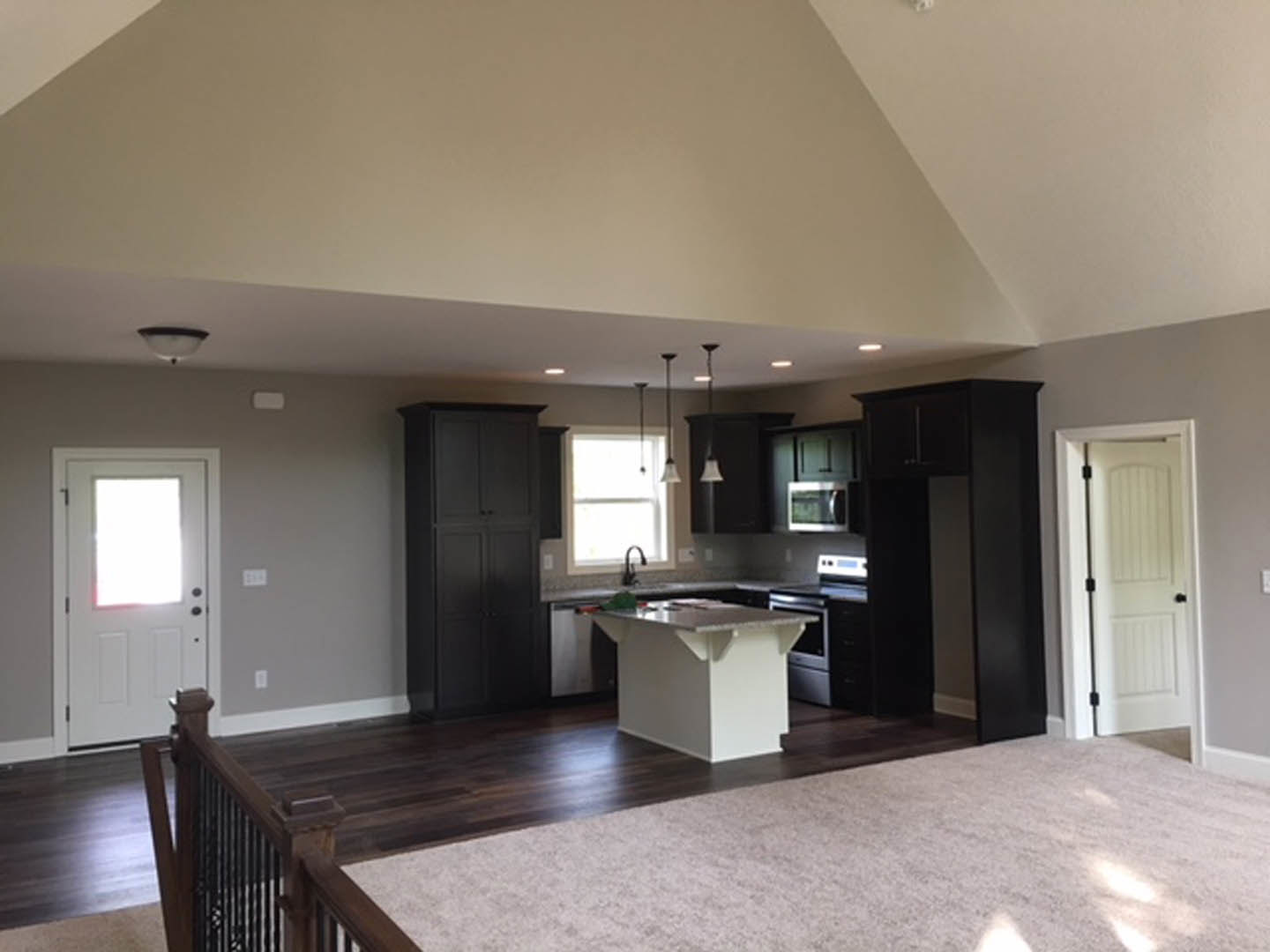 Open-concept kitchen and living room featuring white walls, white door with black knobs and window, white countertop, cabinetry, and light flooring.