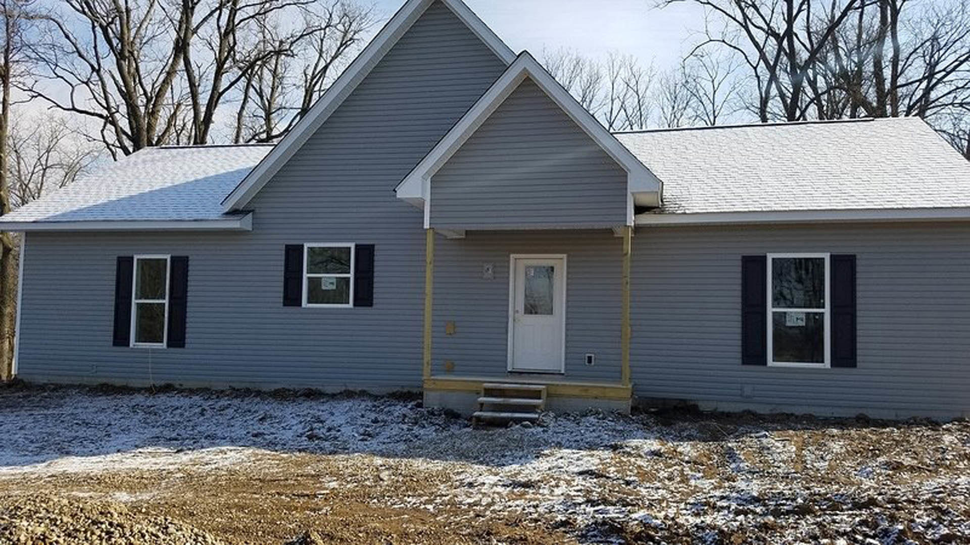 Two-story house with light-colored siding, white-framed windows, and a white front door with a window, surrounded by snow-covered ground and bare trees