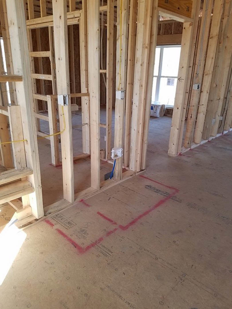 Unfinished room with exposed wood framing, red painted walls, red lines marked on the subfloor, white surfaces, and a roll of toilet paper placed on the floor