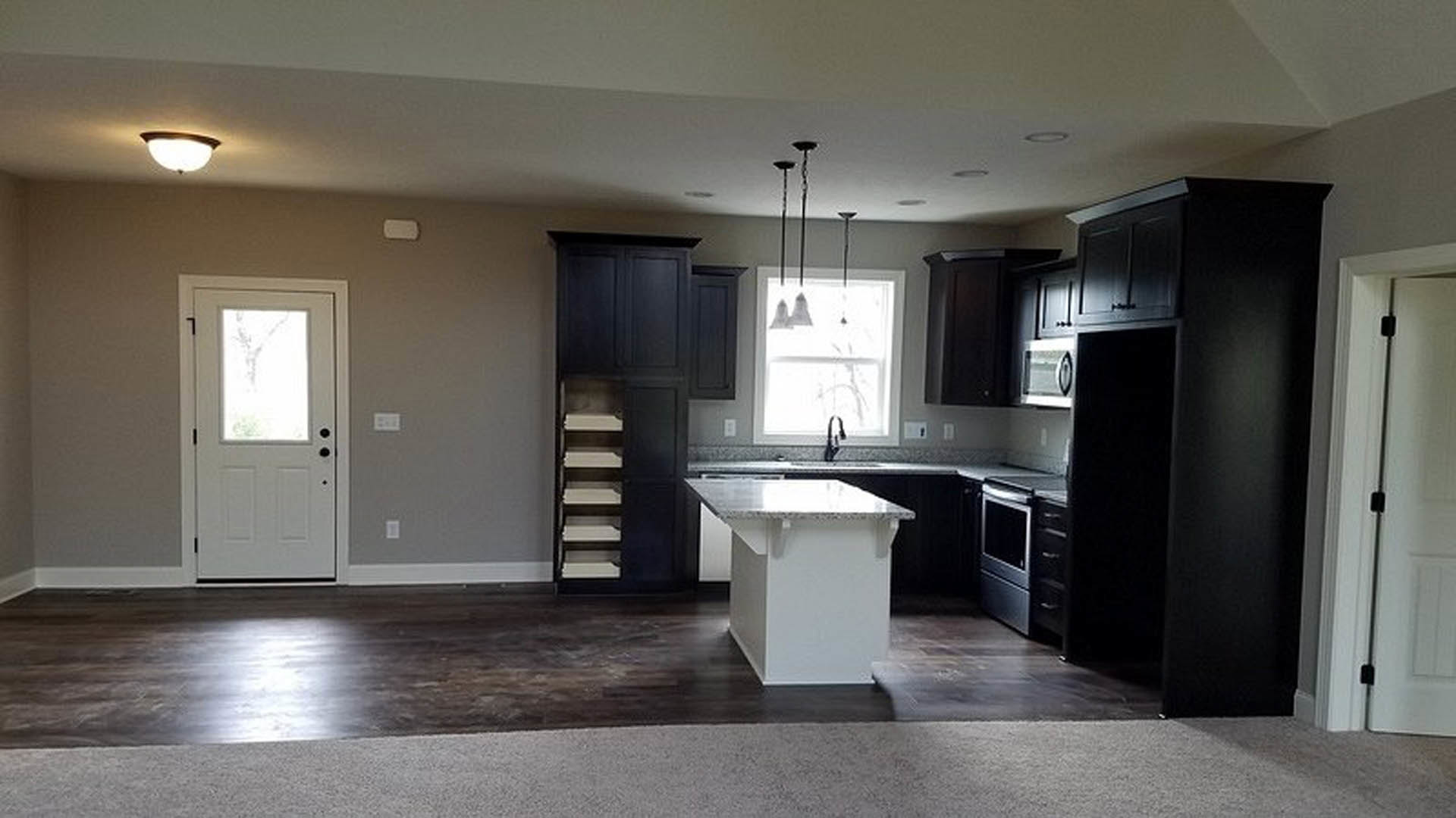 Kitchen with dark wood cabinets, marble-topped white rectangular table, tile flooring, stainless steel sink, white door with glass window, large window letting in natural light