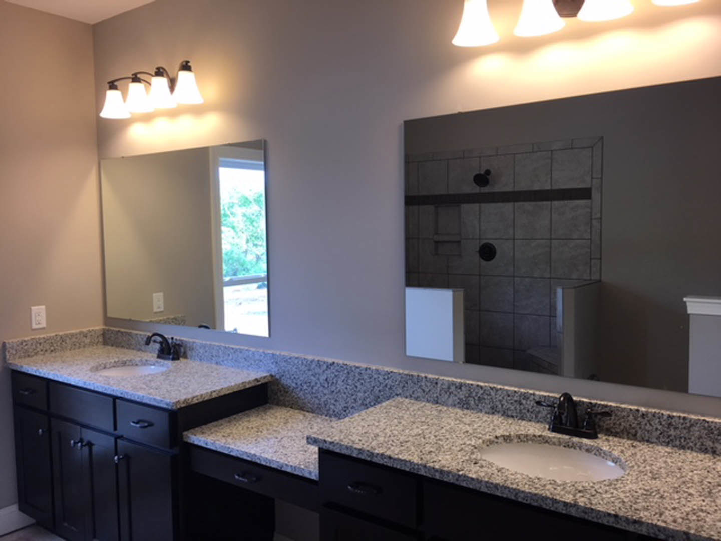 Granite bathroom countertop with undermount sink, large framed mirror, chrome faucet, white cabinetry, and neutral tile backsplash