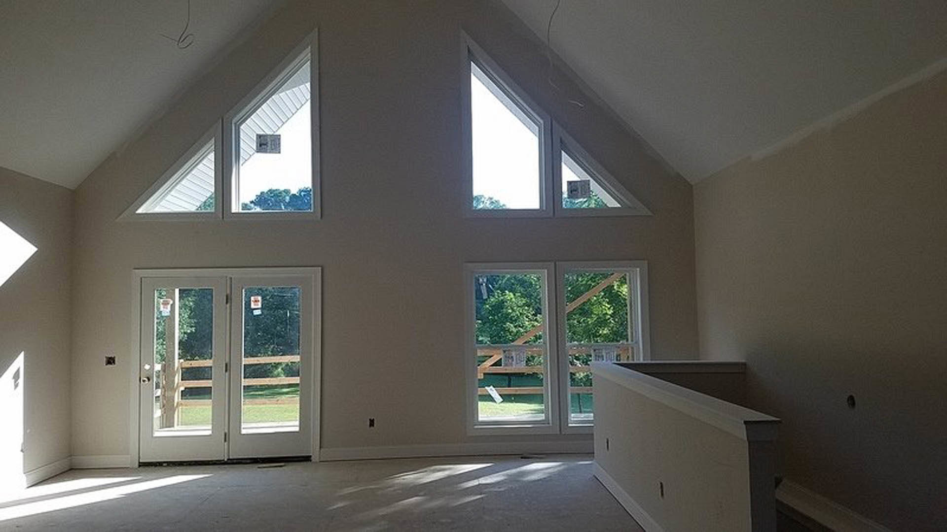 Freestanding white bathtub beneath large windows with tree views, double glass-paneled doors, white walls with black trim, natural daylight highlighting interior molding and