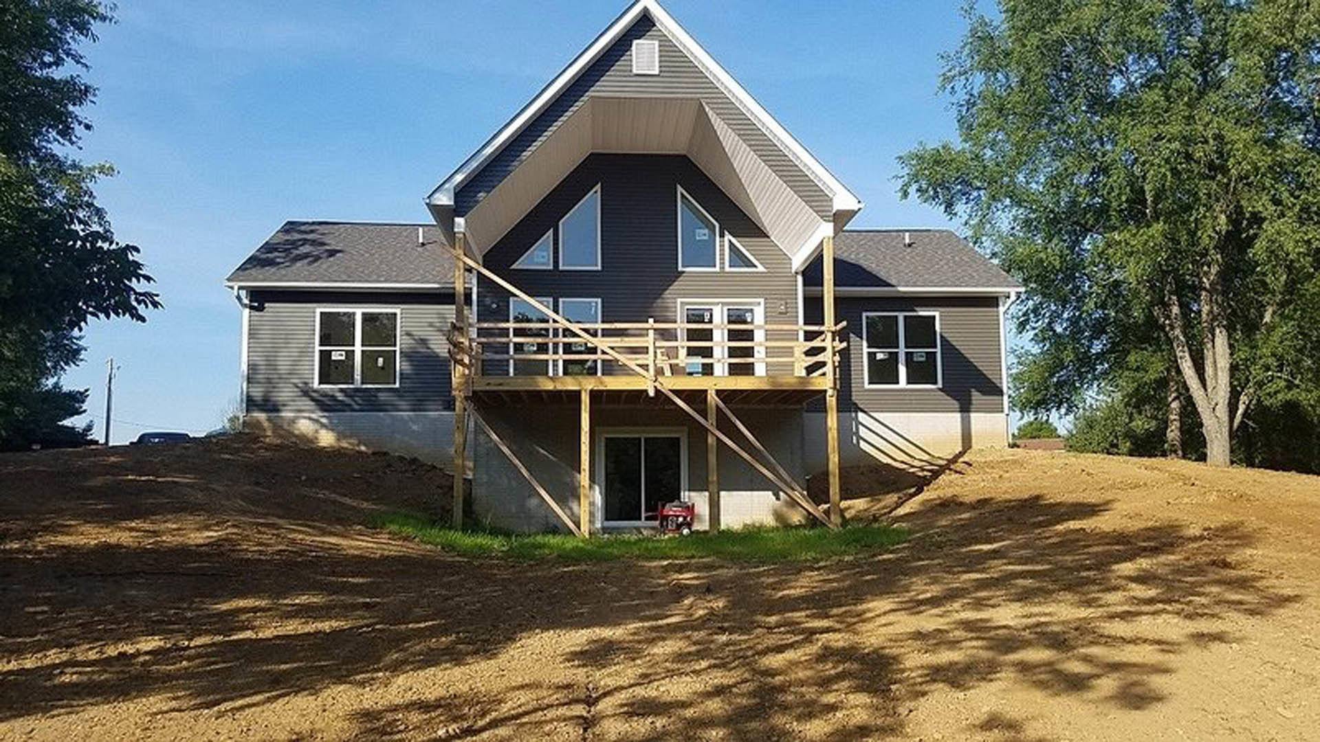 Two-story home with white siding, square white-framed windows, covered front porch, wooden deck, and red tractor parked on the lawn