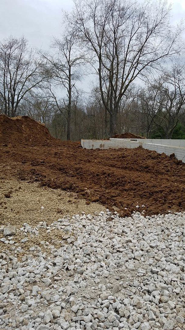 Large mound of dirt and gravel beside bare trees on a winter landscape, exposed soil and rocks in foreground