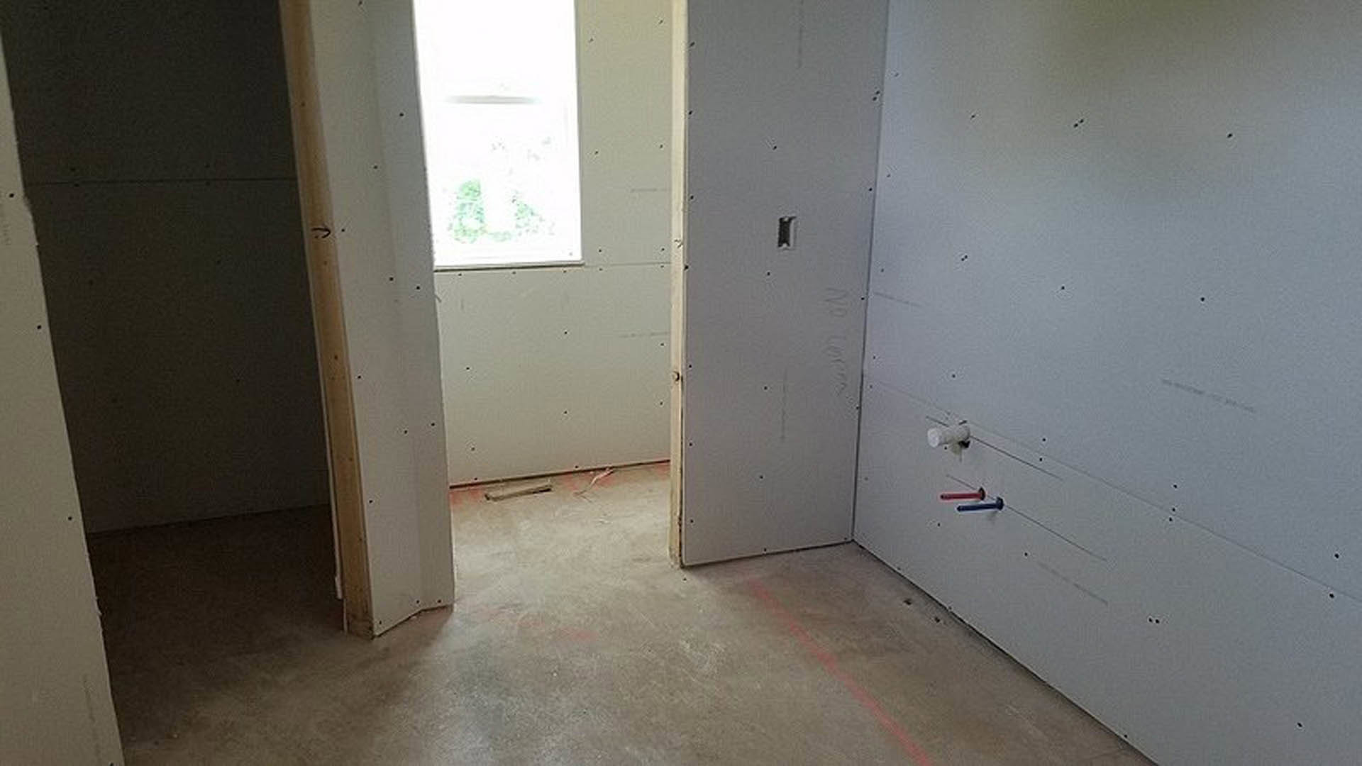 Open white door leading into a room with light-colored plaster walls and wood flooring