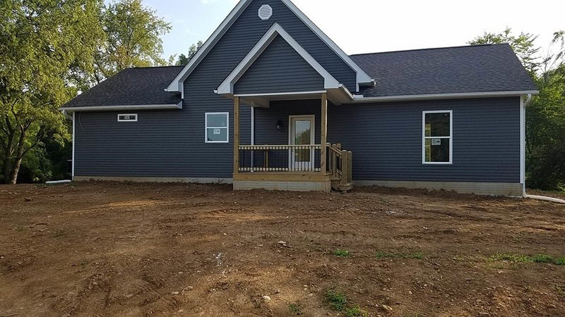 Two-story house with light-colored siding, covered front porch, white-framed windows, white porch railing, and bare dirt yard under a clear sky