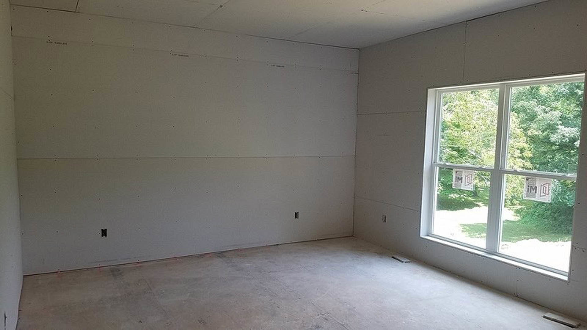 Concrete floor and white plaster wall in a room with large window, daylight streaming in, tree visible outside