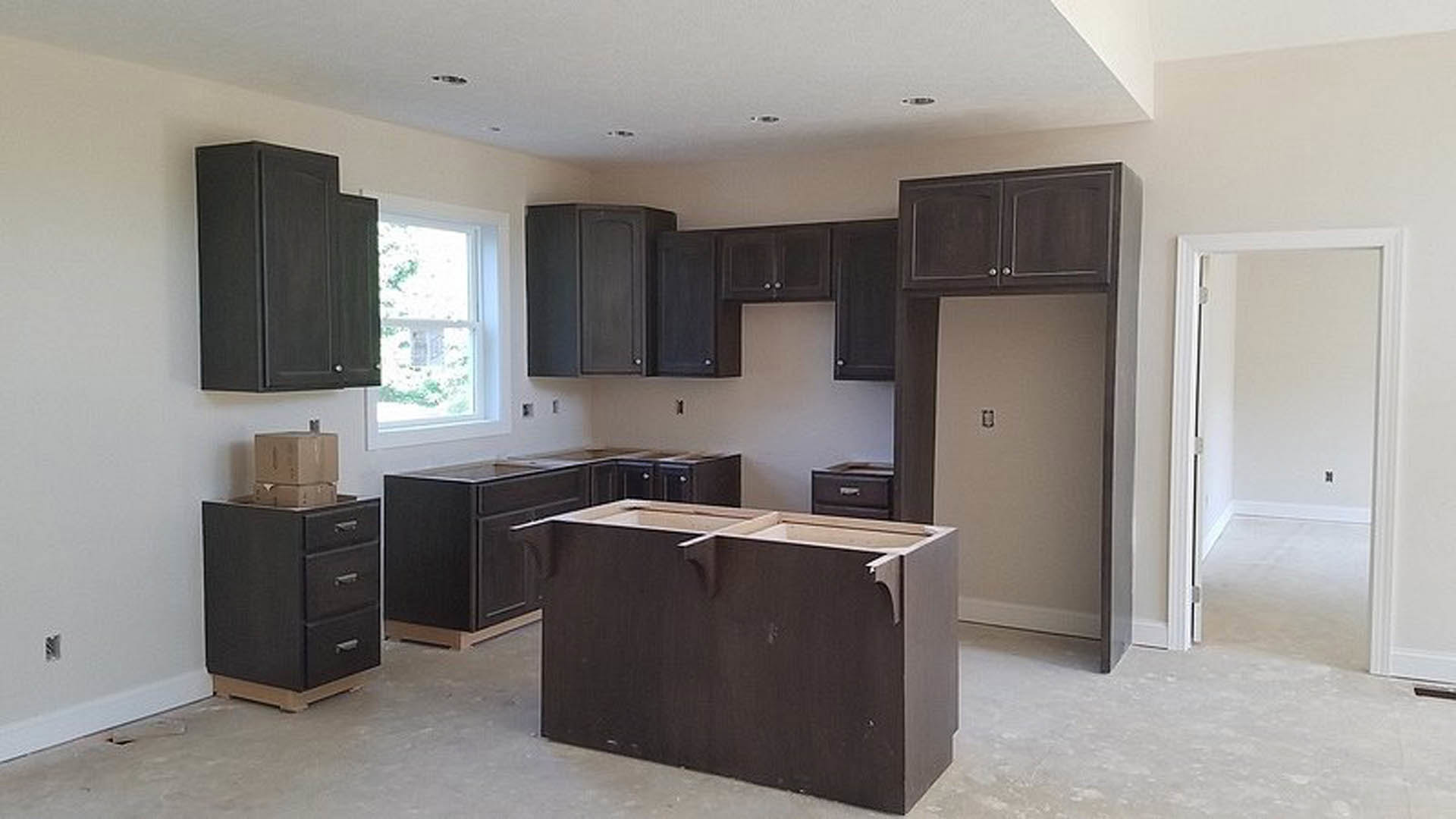 Modern kitchen featuring dark wood cabinets, black lower cabinetry with silver handles, white walls, built-in sink, brown cabinet with decorative holes, and stacked cardboard boxes