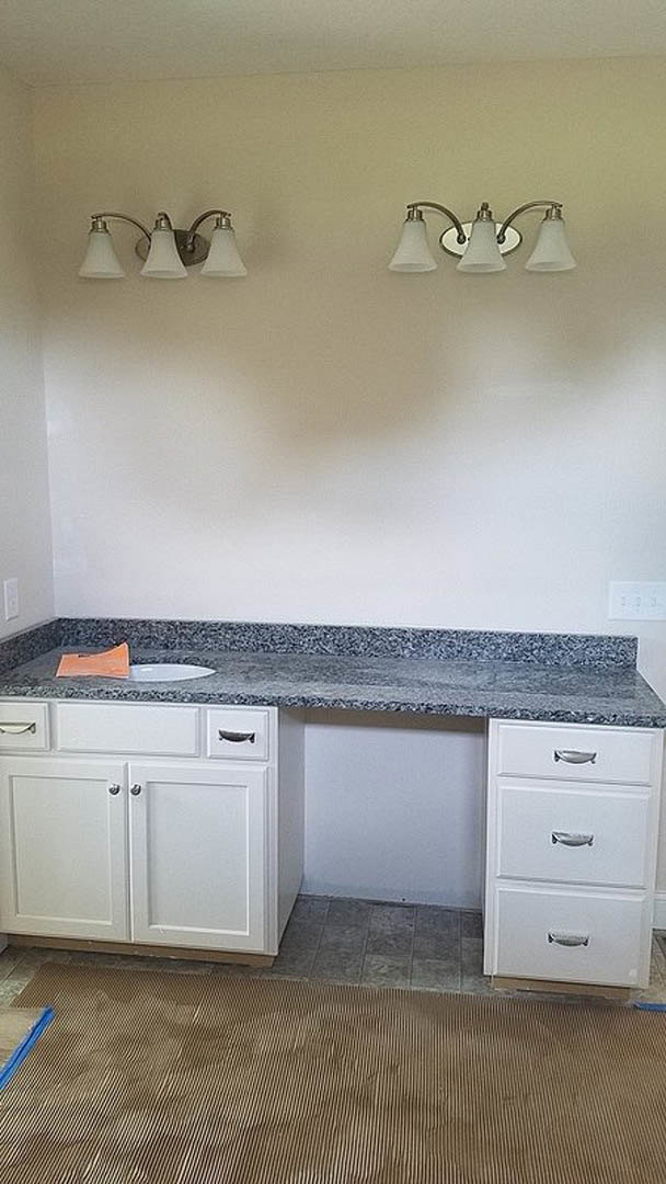 Light-colored stone countertop with stainless steel sink, white tile backsplash, wood cabinetry, and built-in appliances in a modern kitchen.