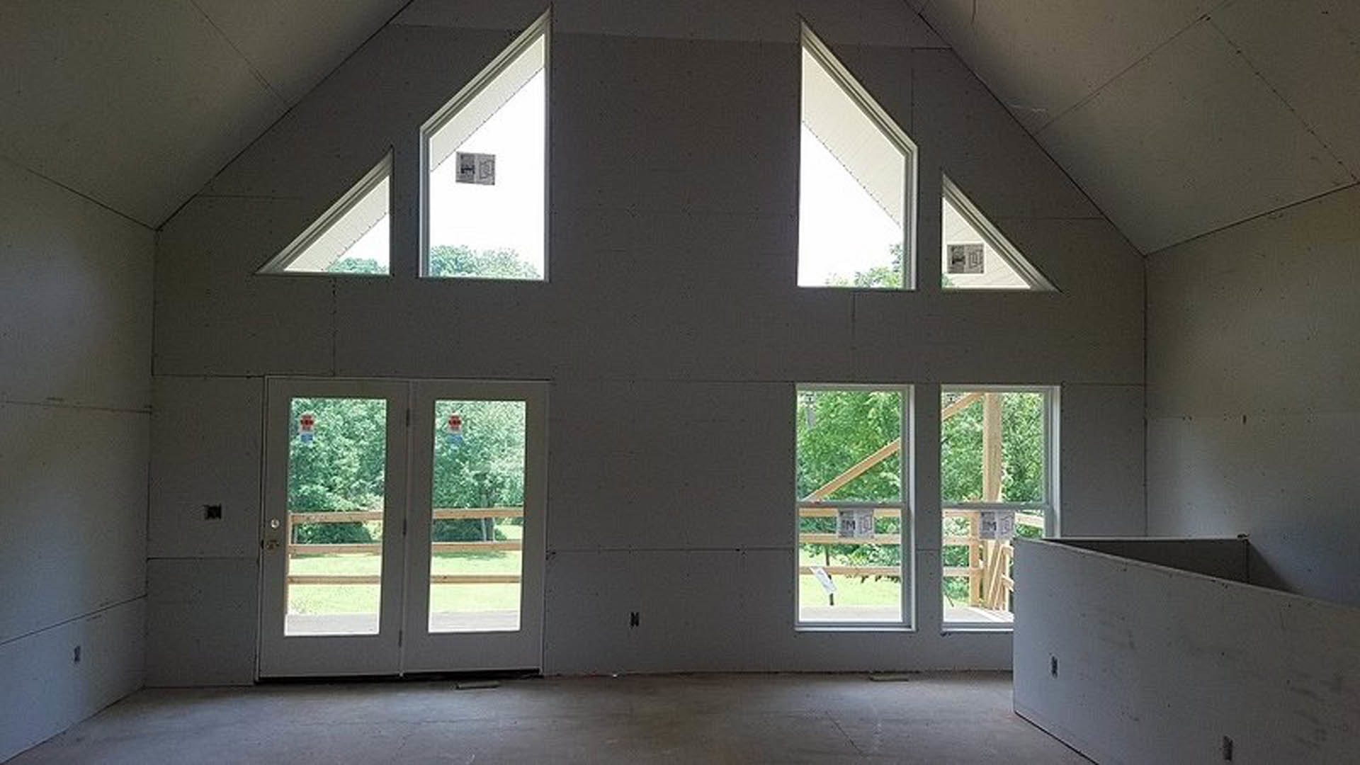 Spacious room featuring double glass-panel doors, large windows with white trim, light hardwood flooring, and smooth white walls.