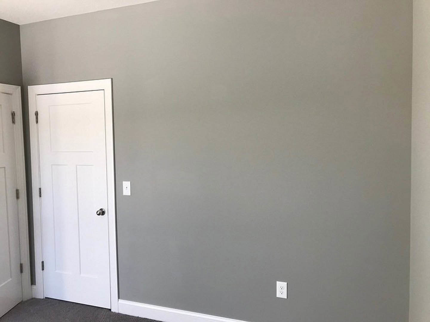 White paneled door with silver metal handle set in a plaster wall, white electrical outlet visible nearby, dark baseboard trim along light-colored floor