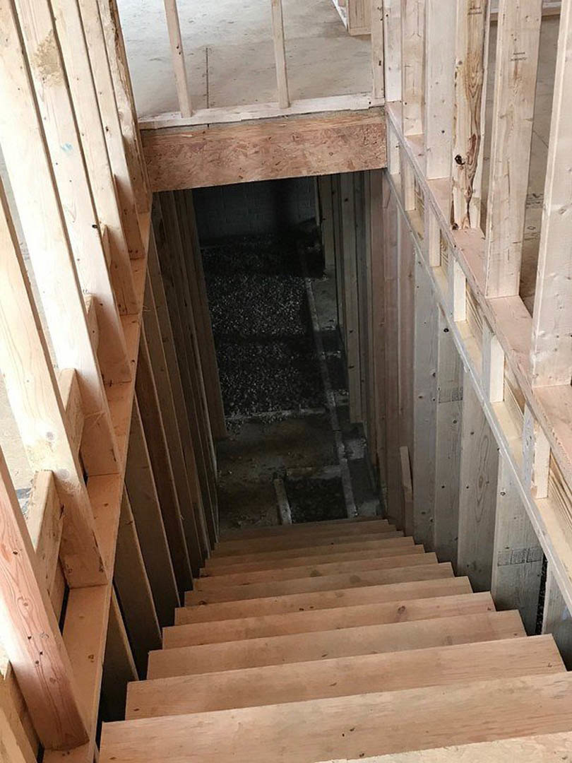 Unfinished wooden staircase with exposed lumber, raw plank steps, and partial handrail in a dimly lit interior under construction