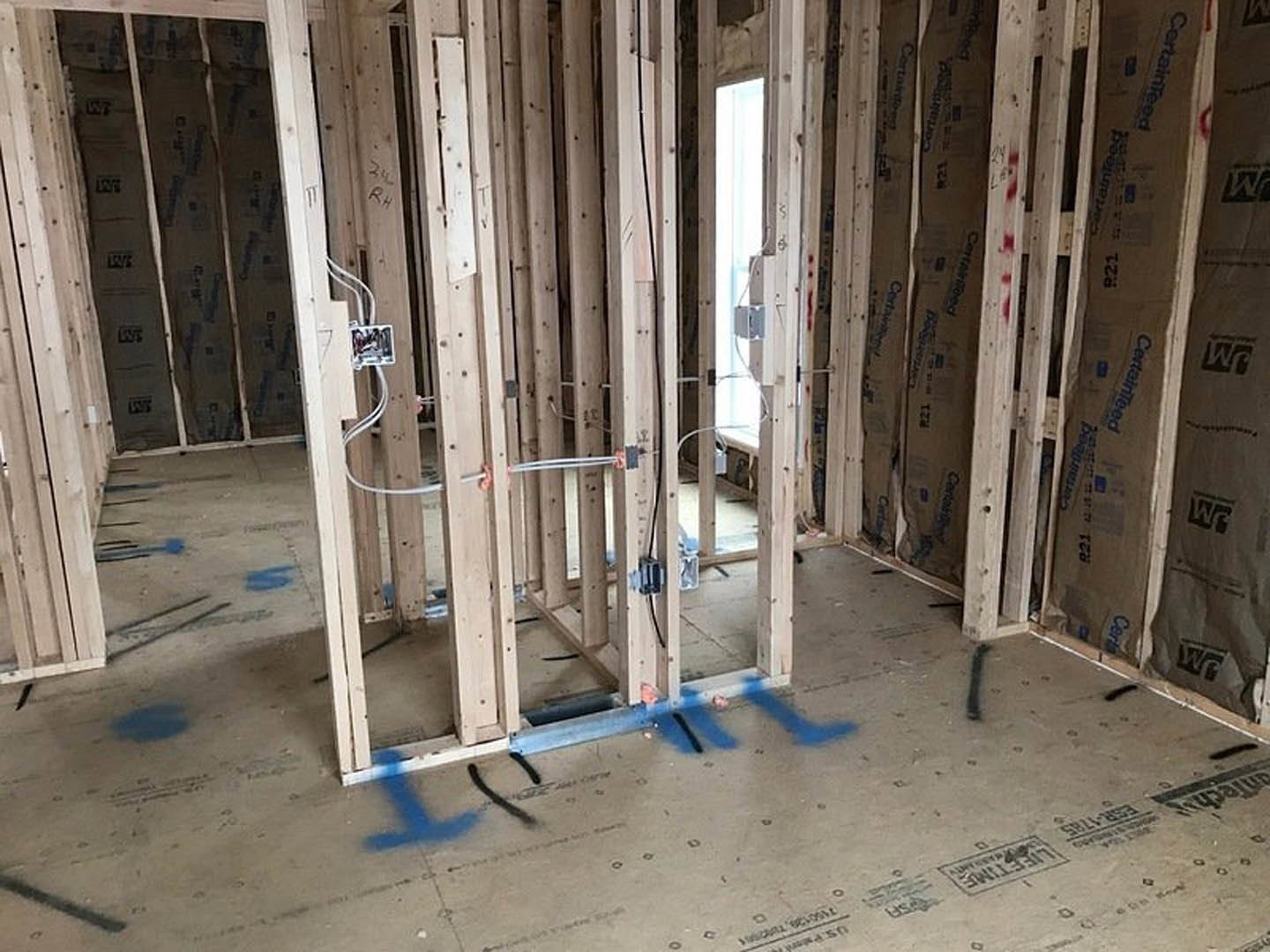 Wood-framed room under construction with exposed beams, electrical wiring, and blue-painted walls