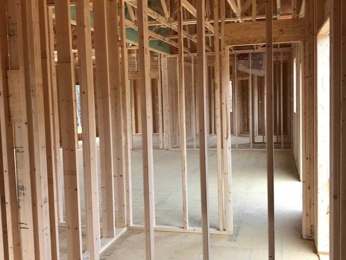 Wood framing and exposed beams in a partially constructed room with a concrete floor and a window
