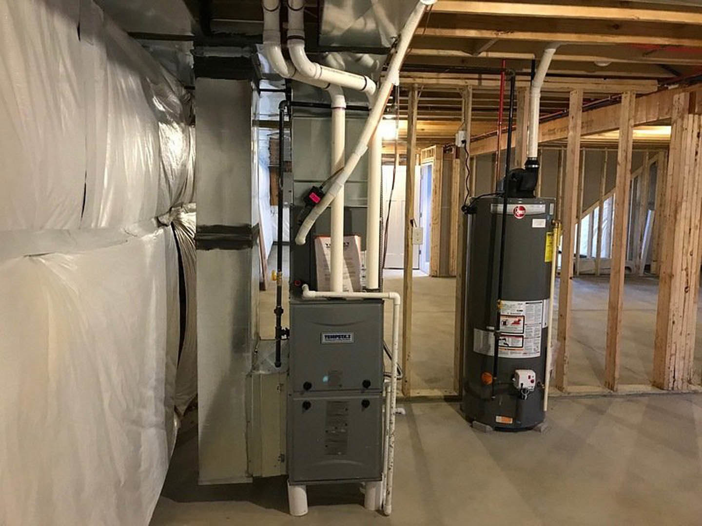 Black steel boiler cylinder installed against a white wall in a utility room with light-colored flooring and visible ceiling pipes