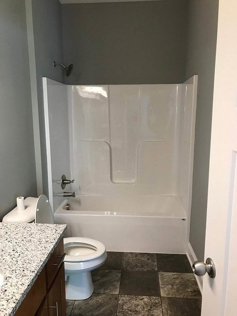 Bathroom with white freestanding bathtub, white toilet with closed lid, light-colored tile flooring, and neutral walls