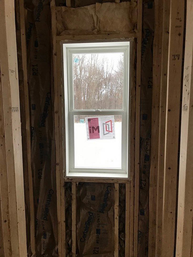 Large wood-framed window set in a neutral wall, sunlight filtering into a modern room with visible paper taped to the glass.