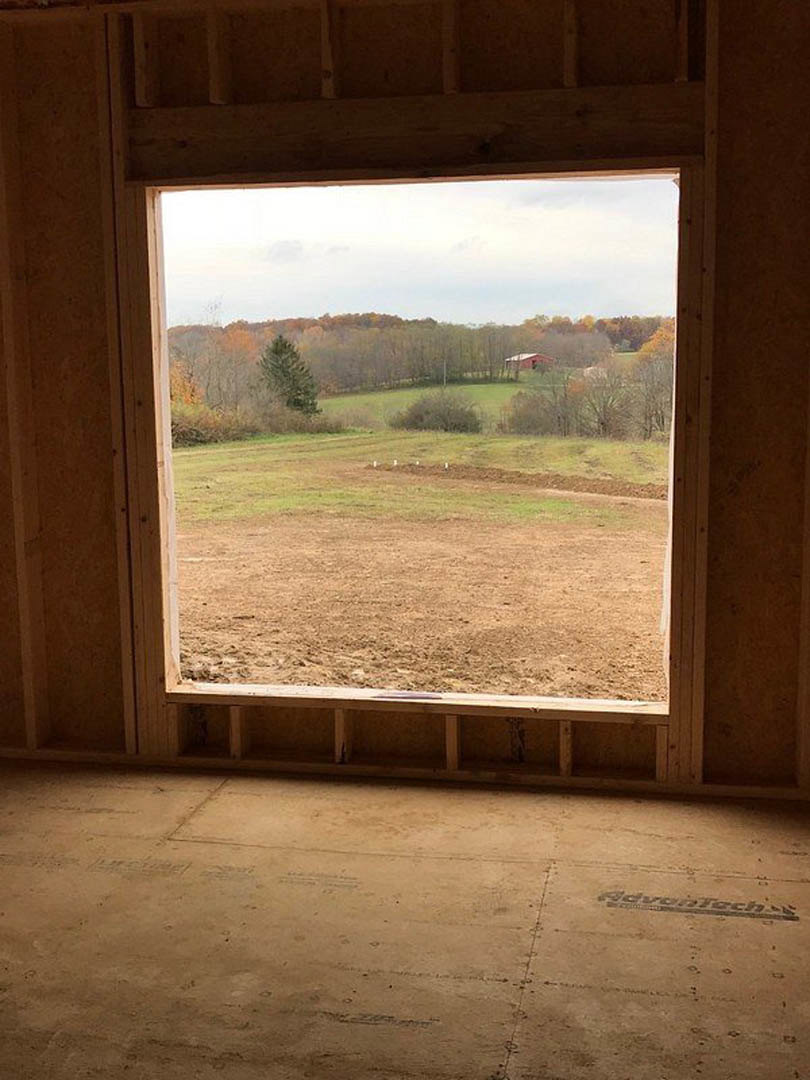 Large window framed by white walls overlooks grassy field and trees, sunlight streaming onto smooth concrete floor in empty room