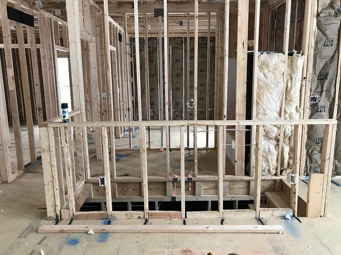 Exposed wooden framing of a house under construction with white insulation material and a blue can resting on a wooden surface