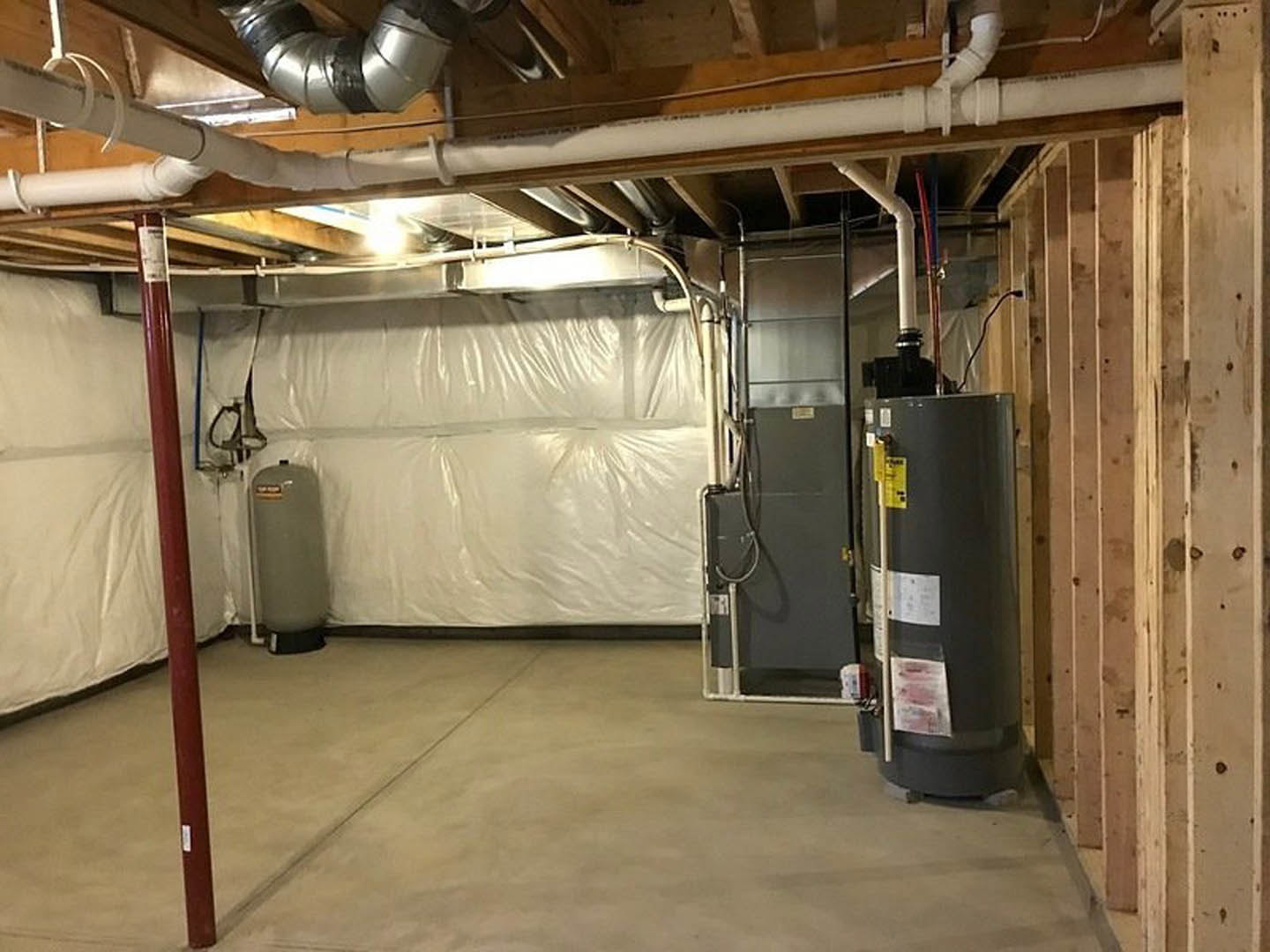 Basement utility room with large grey water tank, exposed white wall, ceiling beams, and building insulation