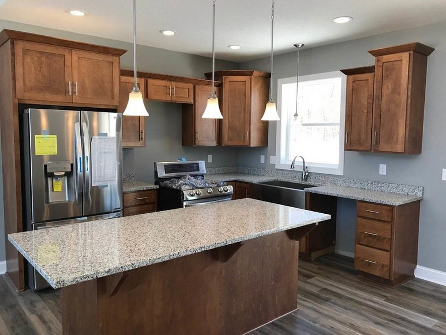 Granite countertops, stainless steel stove, white cabinetry, refrigerator with papers, window with natural light, undermount sink, neutral wall colors