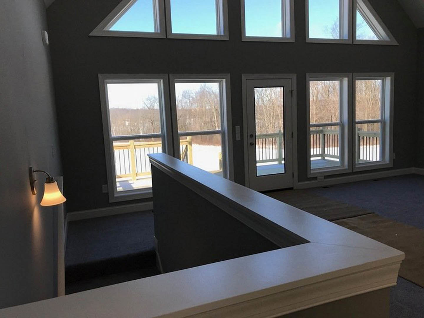 Open living area featuring white countertops, glass-paneled doors leading to a deck, large windows, and a modern light fixture with a fabric shade.