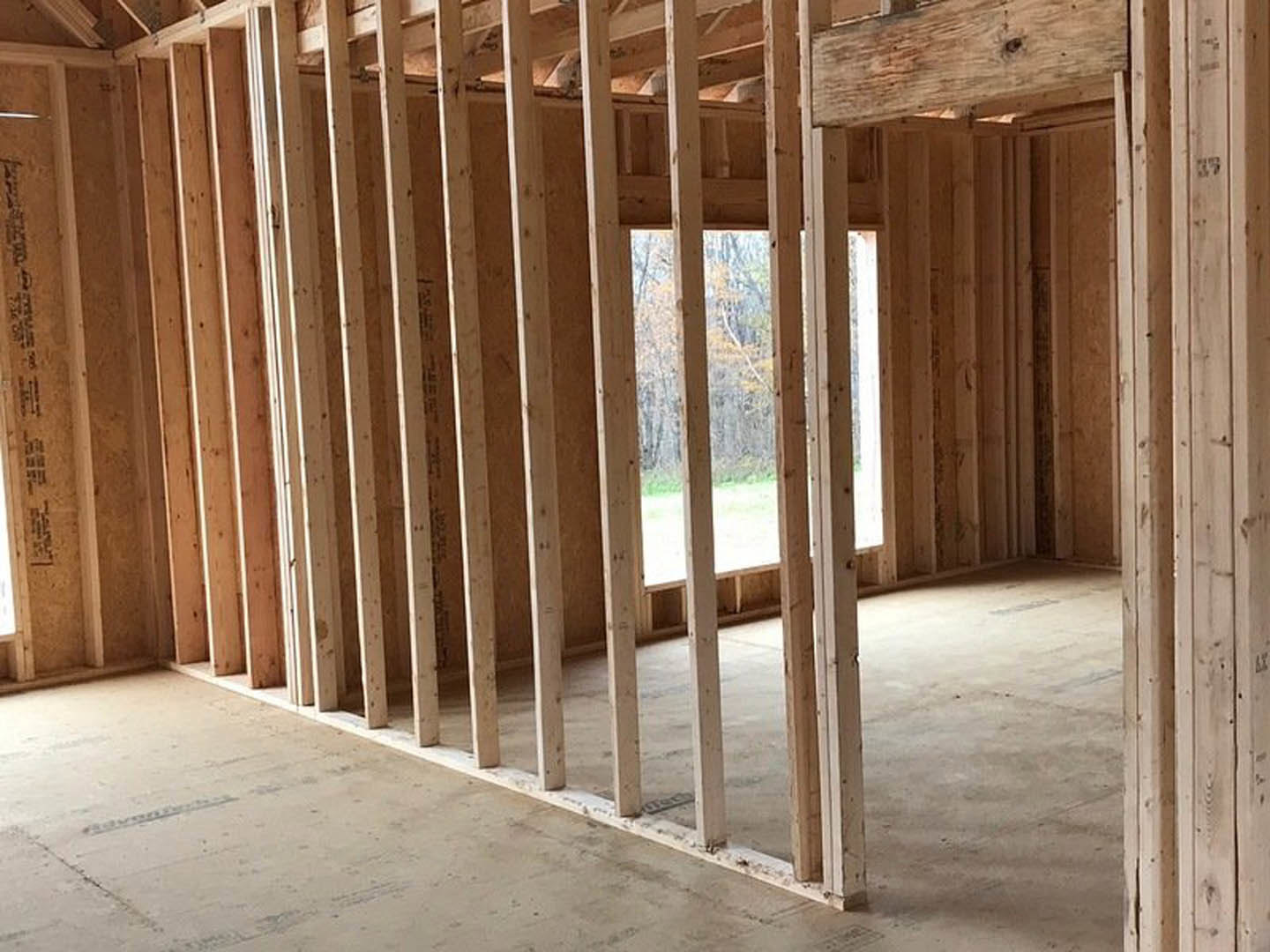 Living room with exposed wood ceiling beams, large window framed in wood, light-colored walls, and hardwood flooring