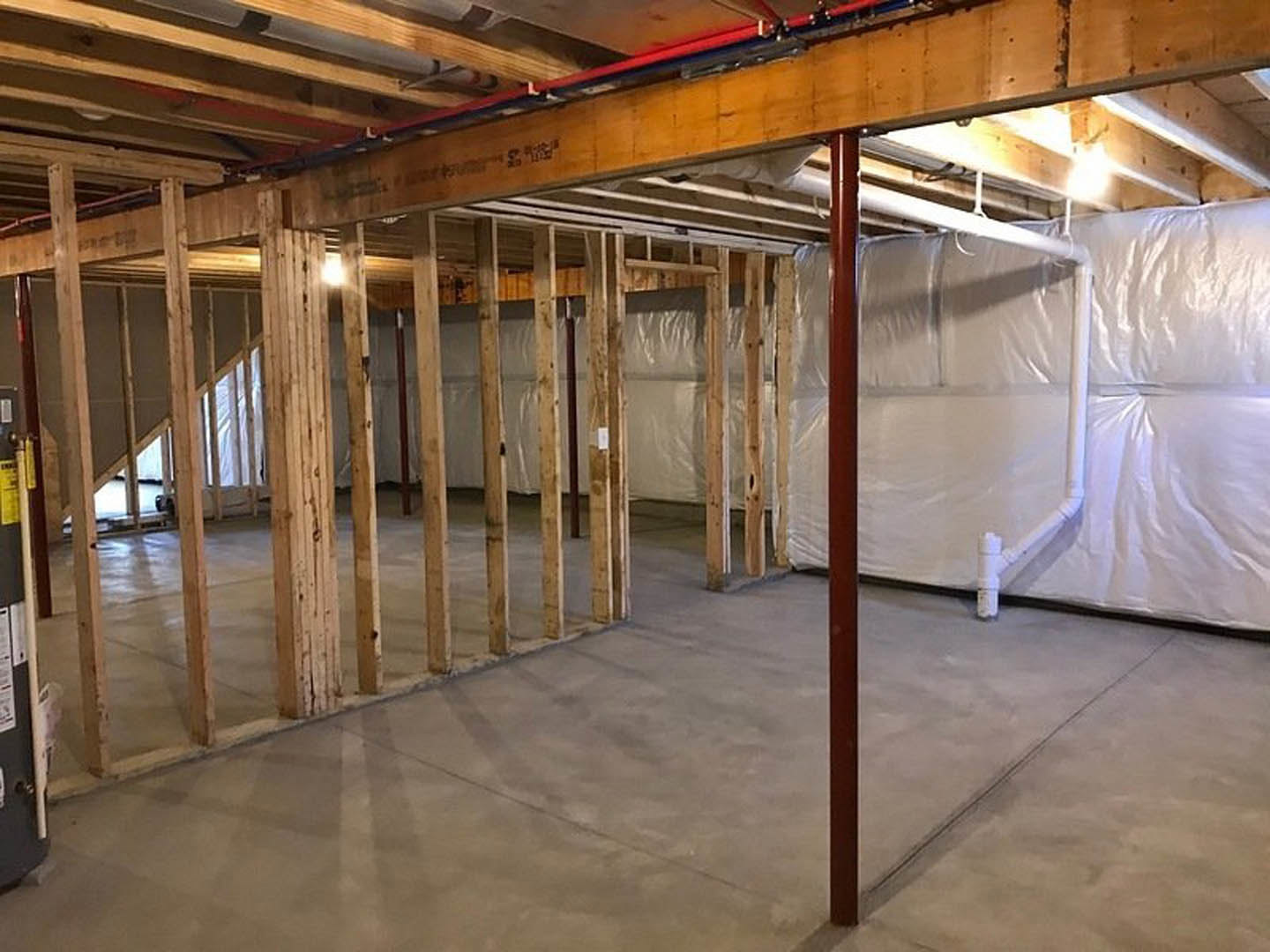 Basement room with exposed wood beams, white walls, unfinished concrete floor, and a red support pole