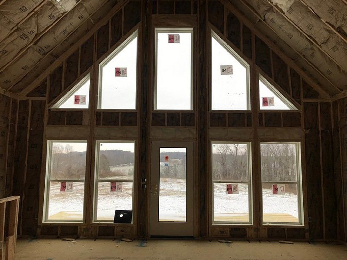 Sunlit room with large wood-framed windows, white walls, and a wooden door opening to a snowy field