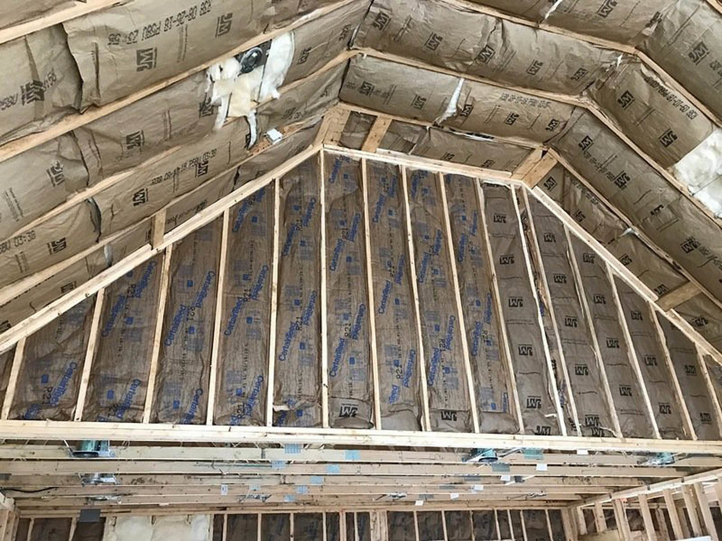 Exposed wooden ceiling beams with insulation panels, partially finished roof structure inside a home under construction, white cat sitting beneath the ceiling, close-up of window