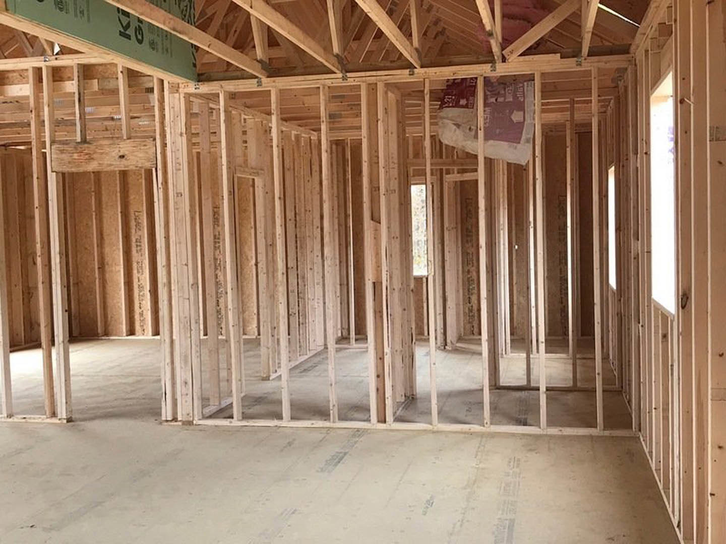 Unfinished room with exposed wood framing, ceiling beams, construction materials, and a green sign attached to the structure