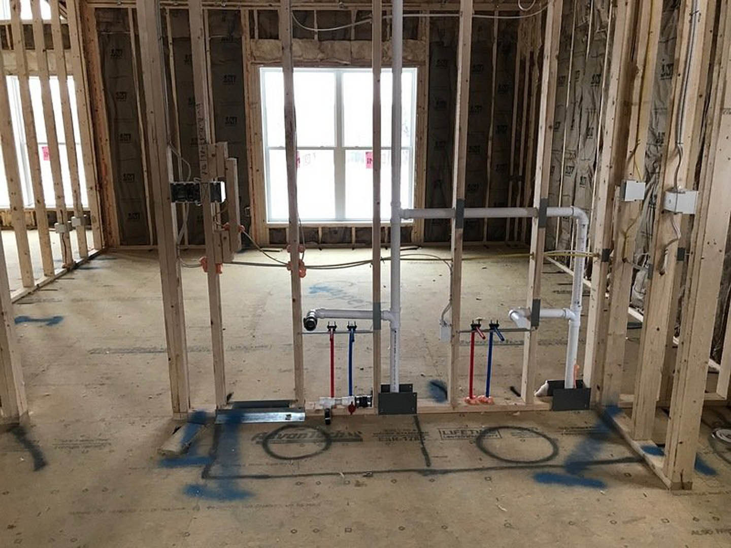 Unfinished room with exposed pipes, wooden beams, white-framed window, and construction materials on the floor
