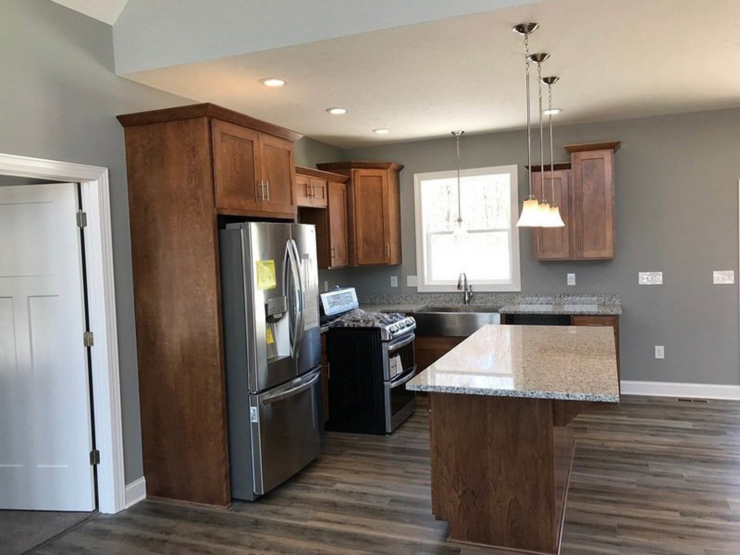 Kitchen with stainless steel refrigerator, wood flooring, white cabinetry, stone countertops, and natural light from a window