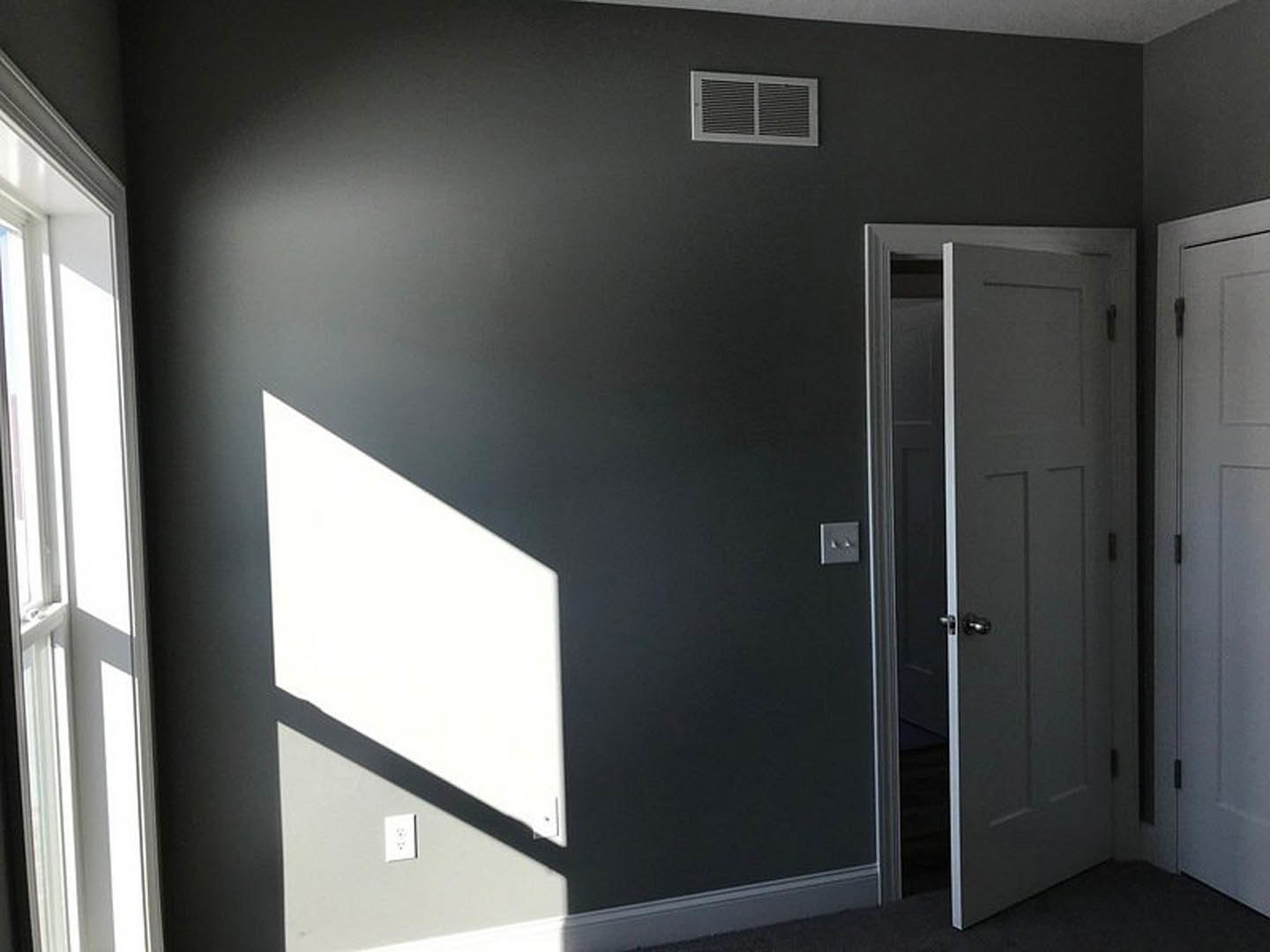 Open white door with brushed metal handle leading into a neutral-toned room, smooth plaster walls, white ceiling, and visible electrical outlet with black markings.
