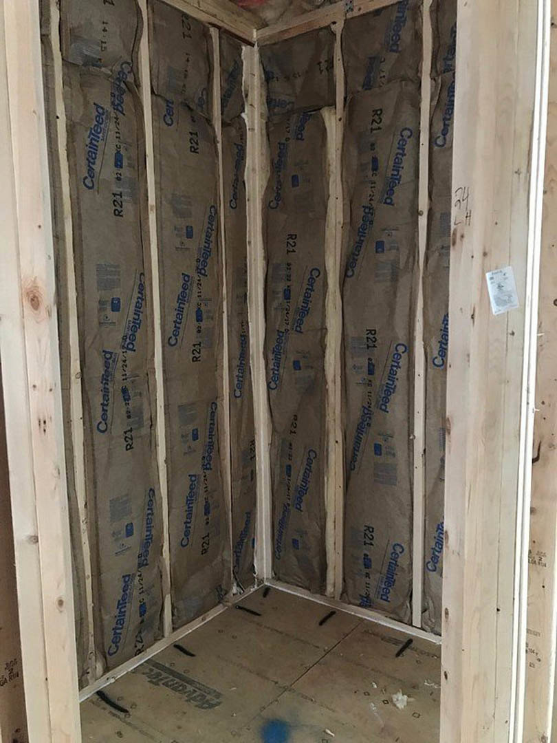 Exposed wood framing and wall insulation in an unfinished room with brown paper bags and a white sheet taped to the wall