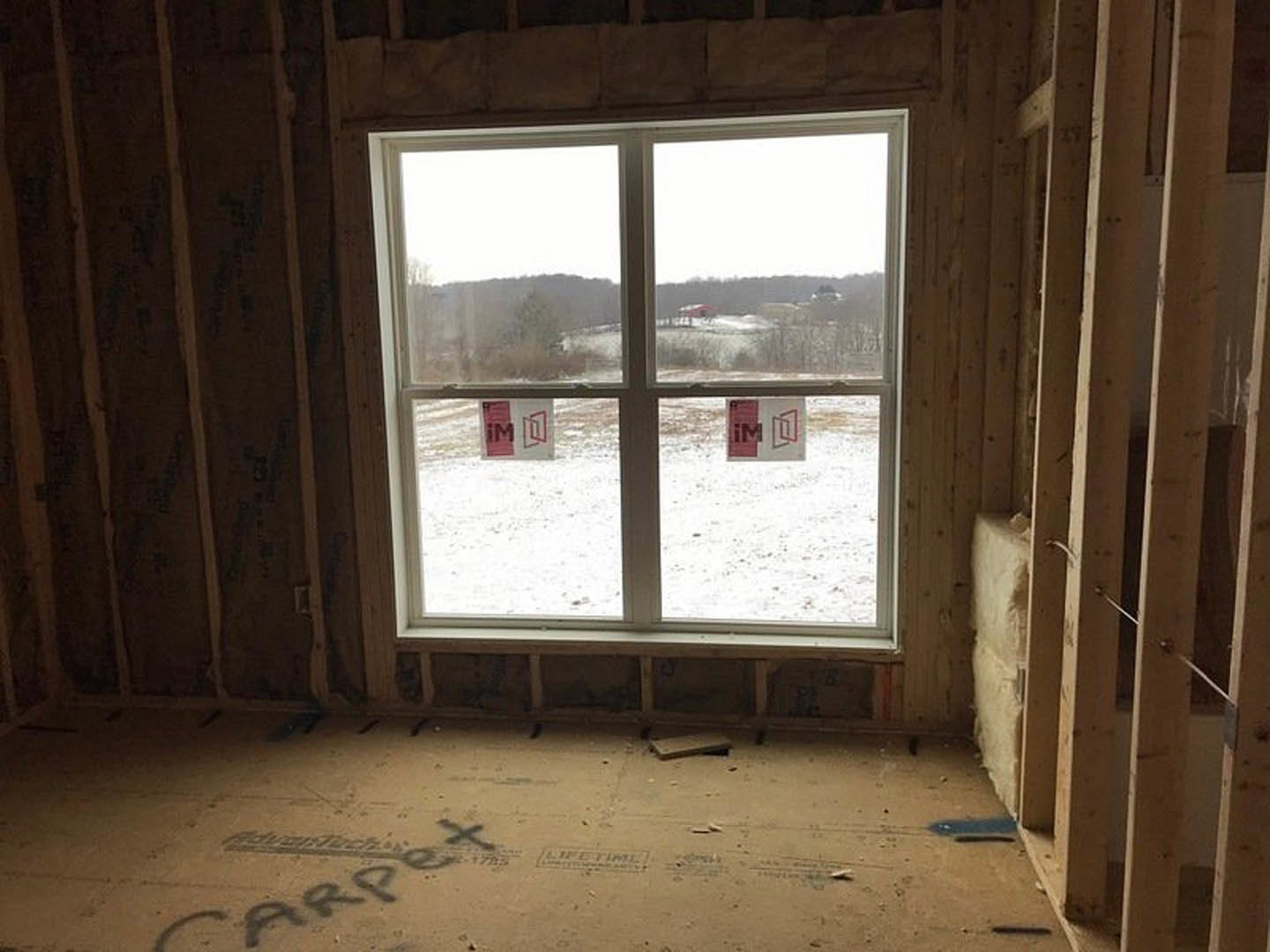 Large window framed by wood, overlooking snowy landscape, concrete floor and wood wall visible inside room