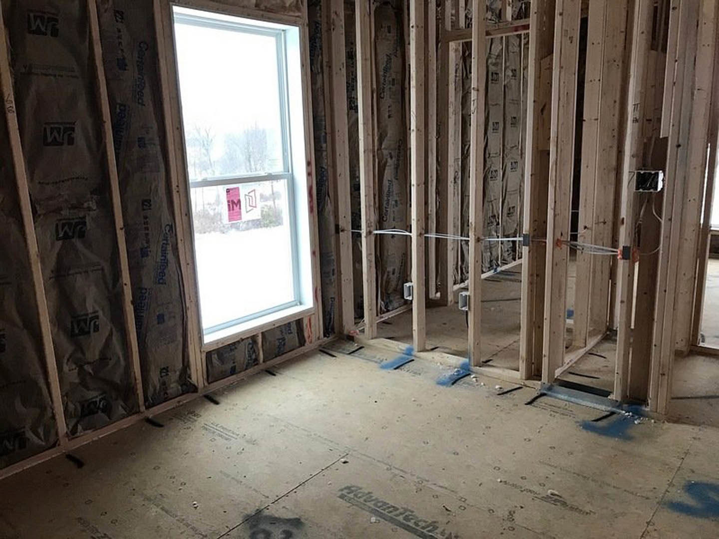 Unfinished room with exposed wood framing, window with pink inspection label, construction materials and insulation visible