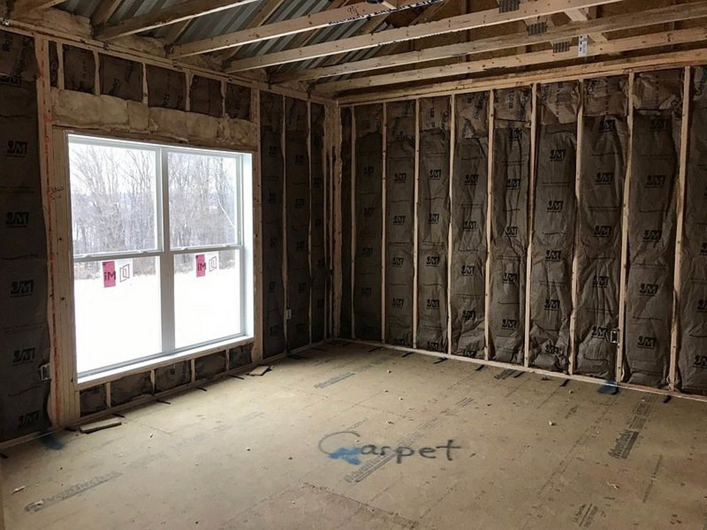 Unfinished room with exposed wall insulation, wood ceiling beams, window, and construction materials scattered on the floor