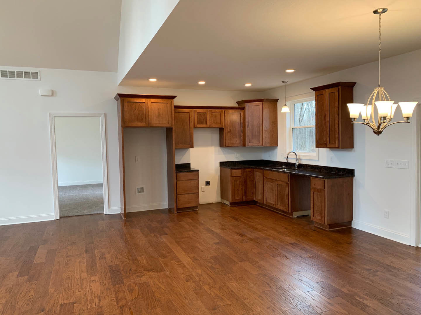 Kitchen with light wood flooring, white cabinetry, stone countertops, stainless steel sink, and modern chandelier overhead