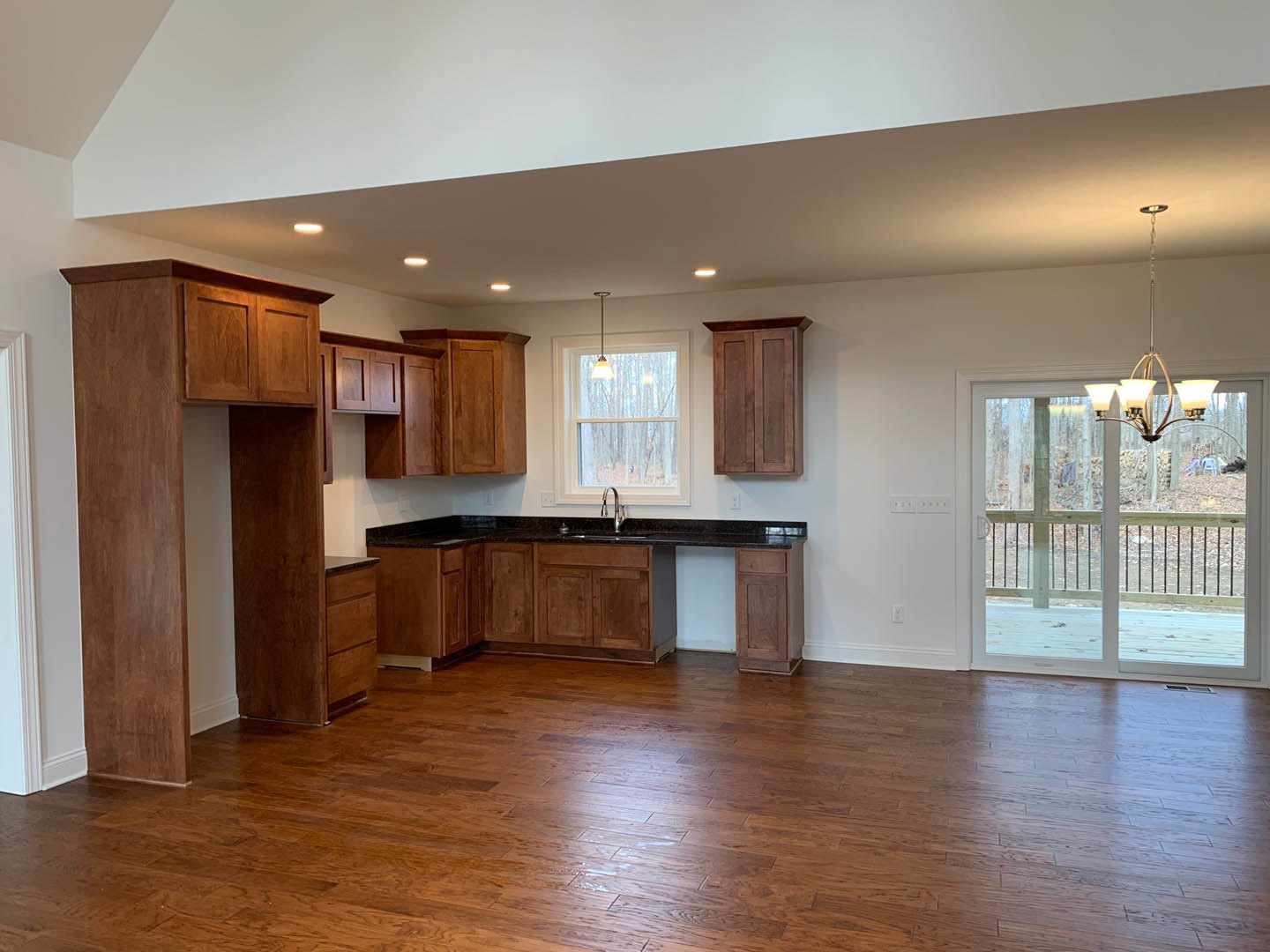 Kitchen with hardwood floors, white cabinetry, stone countertops, sliding glass door, chandelier, and large window with natural light.