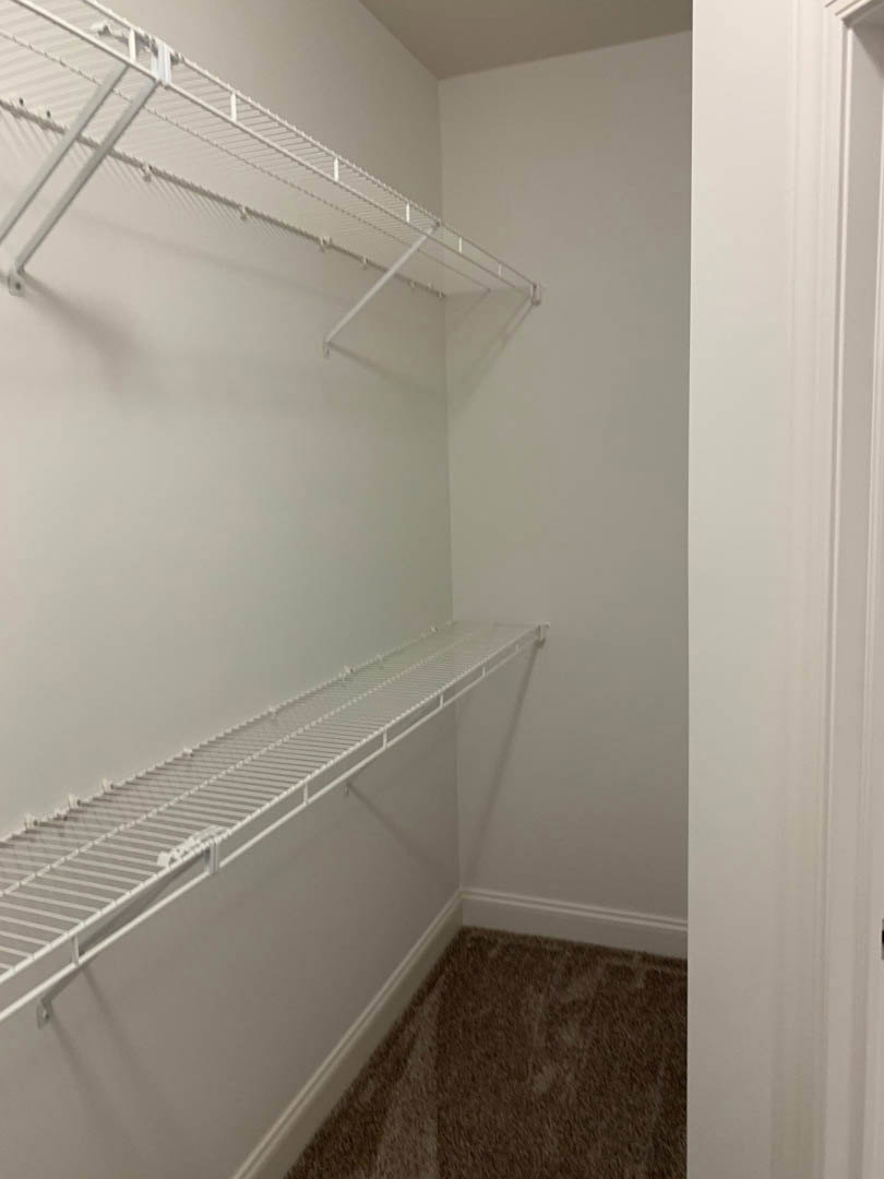 White built-in shelves mounted on a white wall beside a white door with matching trim, carpeted floor, and plaster ceiling in a residential room.
