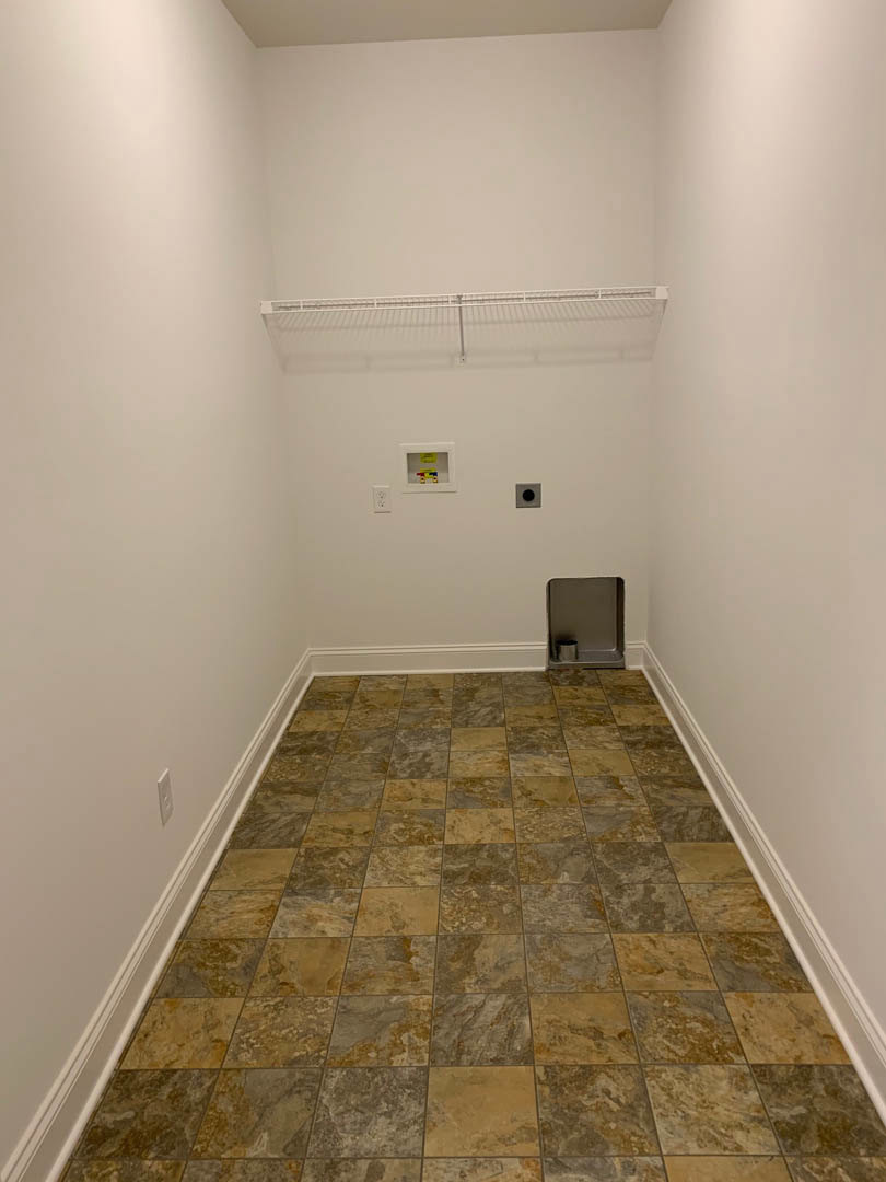 Bathroom with brown and tan tile flooring, metal trash can beside plaster wall, metal railing mounted above, white storage box with toy on metal shelf