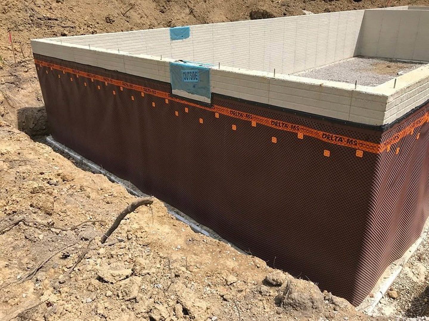 Concrete slab foundation with wooden framing, blue vapor barrier, and construction signage on sandy ground