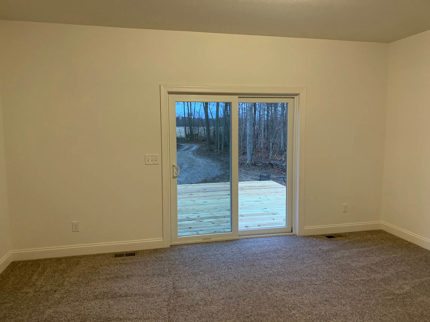 Carpeted room with sliding glass door opening to wooden deck and view of trees