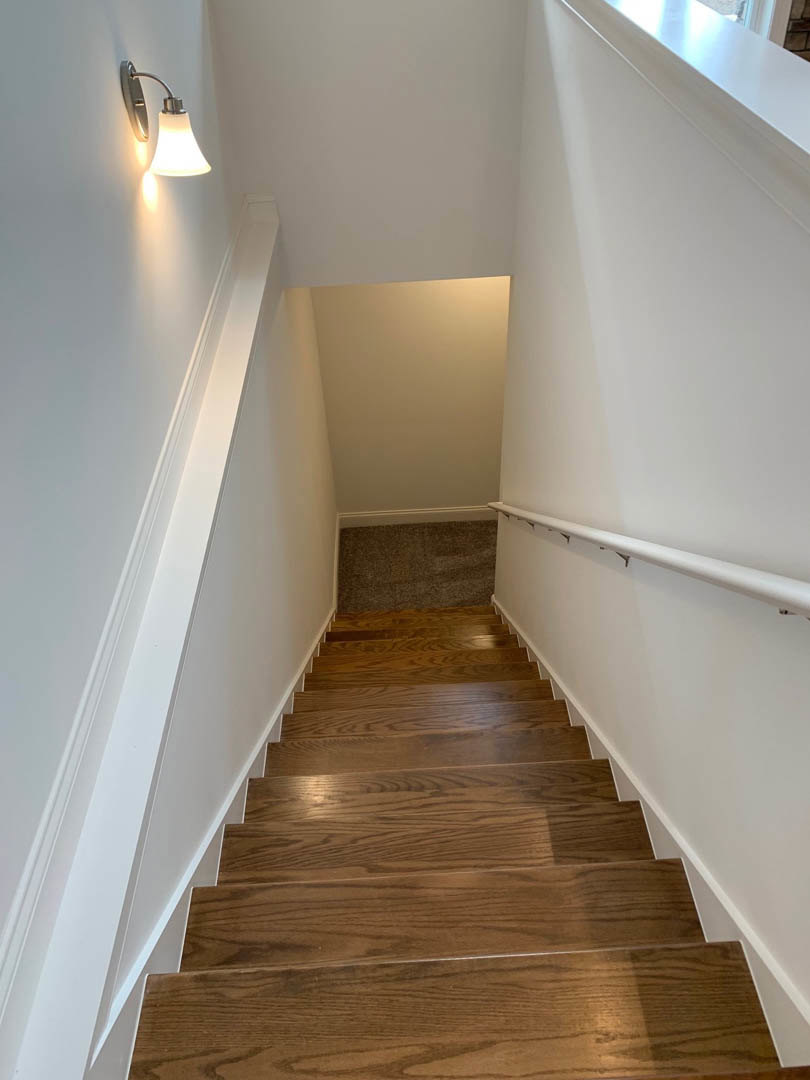 Wooden staircase with white plaster walls, carpeted flooring, and a wall-mounted lamp illuminating the stairwell.
